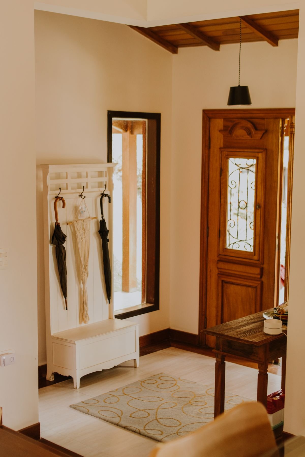 Bright entryway with wall-mounted coat hooks, umbrellas, a small storage bench and a wooden front door