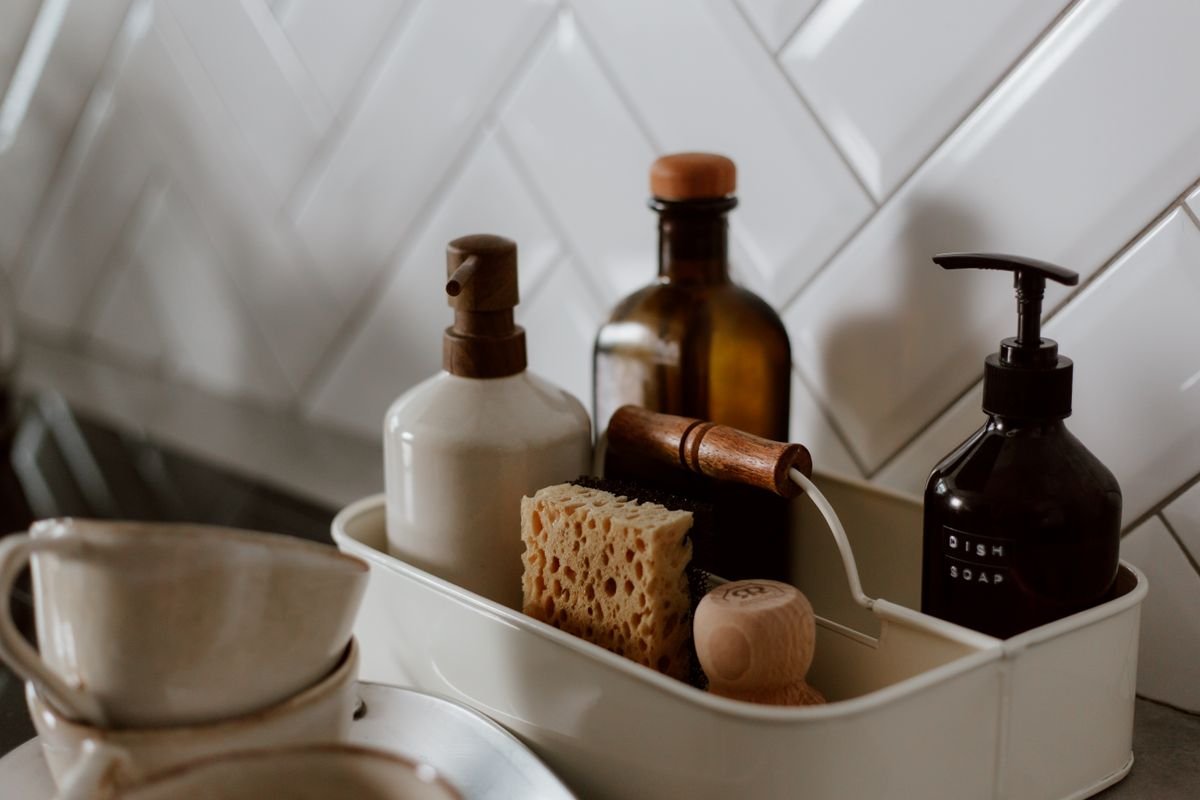 A metal caddy holding dish soap, a sponge and a scrub brush beside a white tiled backsplash