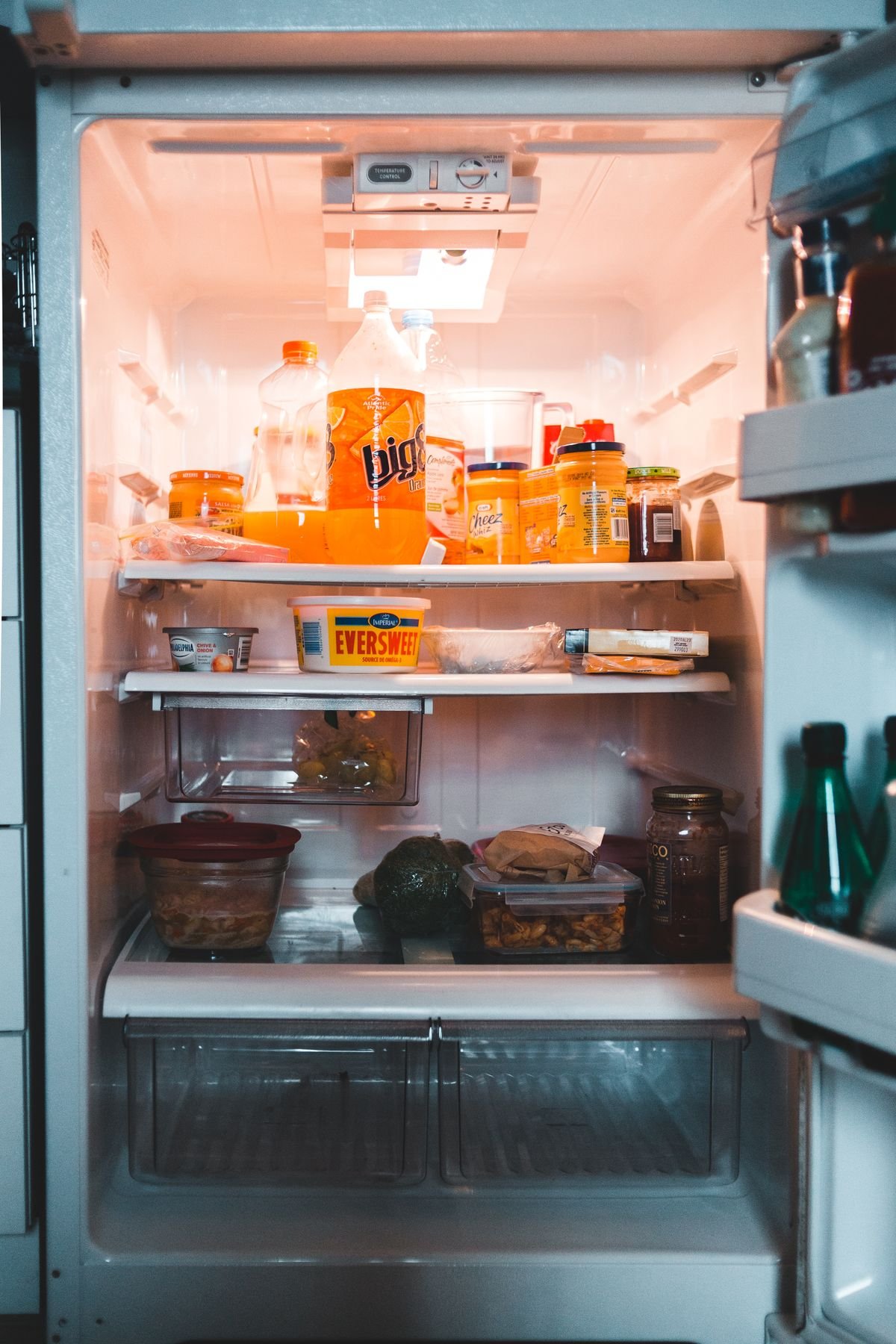 Open refrigerator with drinks, condiments and leftovers on its shelves