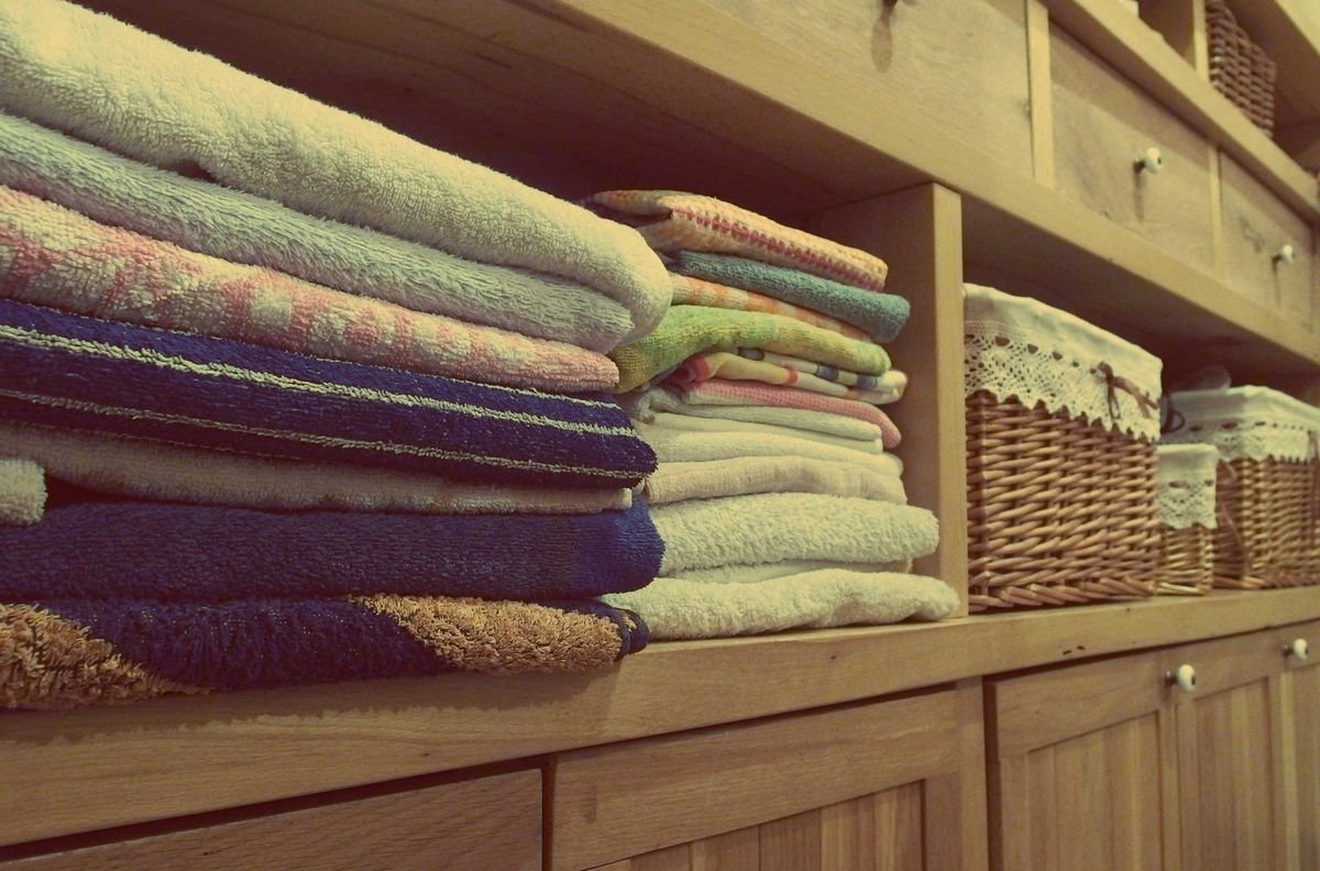 Folded bath towels stacked on wooden shelves next to woven storage baskets in a linen closet