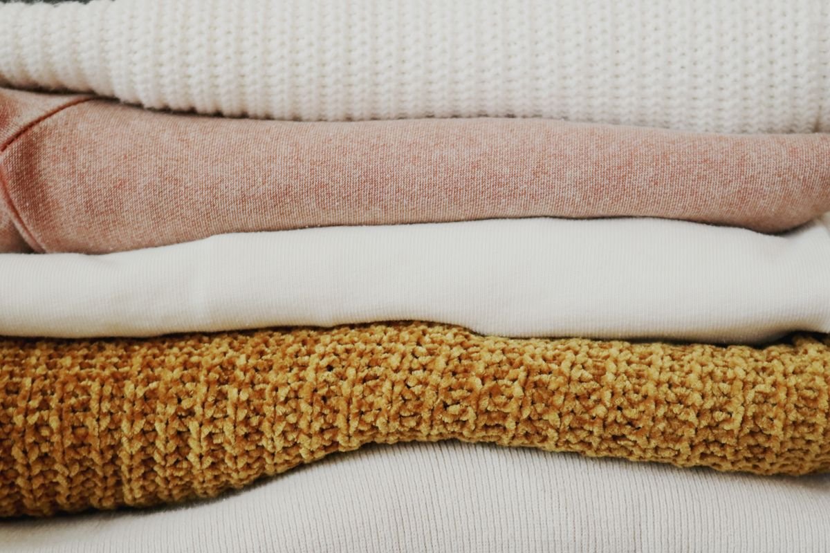 Stack of neatly folded knit throw blankets in cream, pink and mustard tones