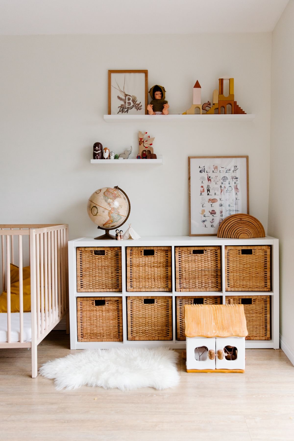 Bright nursery with a white cube shelf holding woven storage baskets, a crib and floating shelves with wooden toys